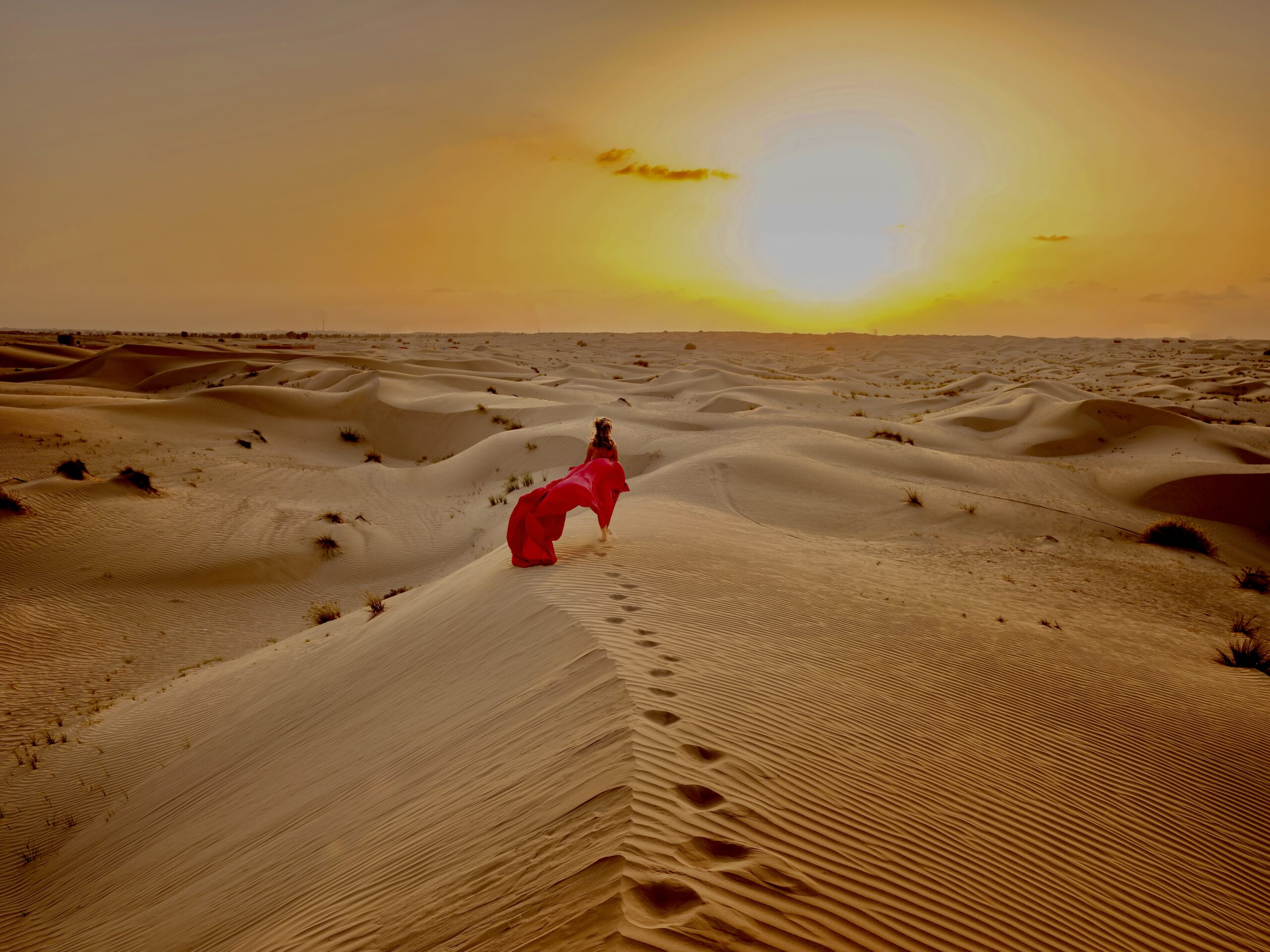 Desert adventure. Young arabian Woman in red silk dress in sands dunes of UAE desert at sunset, fantastic view. The Dubai Desert Conservation Reserve, United Arab Emirates.
